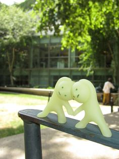 two small plastic elephants on top of a metal rail in front of some trees and people