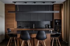 a kitchen with wooden cabinets and black counter tops, along with bar stools that match the wood flooring