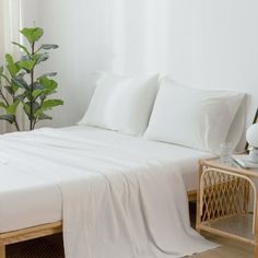 a bed with white sheets and pillows next to a potted plant on a side table