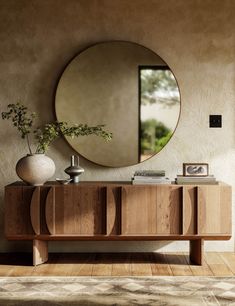 a round mirror on the wall next to a wooden cabinet with vases and books