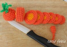 a crocheted carrot sitting on top of a cutting board next to a knife