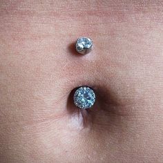 two diamond studs sitting on the side of a woman's stomach, one is white and the other is light blue