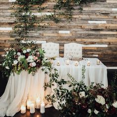 a table with candles, flowers and greenery is set up in front of a wooden wall