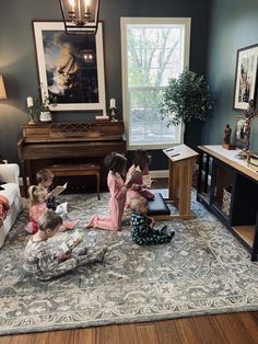 three children are sitting on the floor reading books in front of a piano and fireplace