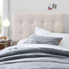 a bed with white linens and pillows in front of a wall mounted light fixture