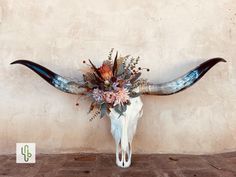 a cow skull with flowers on it's head is displayed against a stucco wall