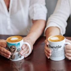 two people holding coffee mugs with the words bestie on them sitting at a table