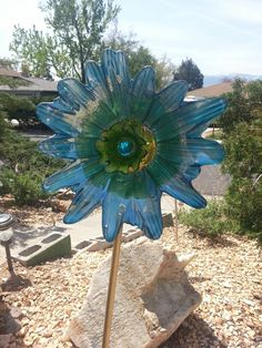 a blue glass flower sitting on top of a rock in the middle of a garden