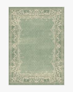 a green rug with white flowers and leaves on the border, in front of a gray background