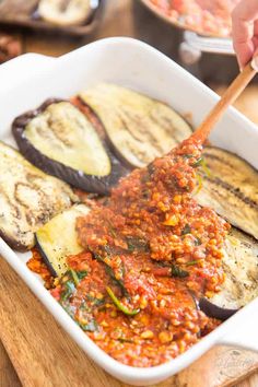 someone is dipping some food into a casserole dish with zucchini and other vegetables