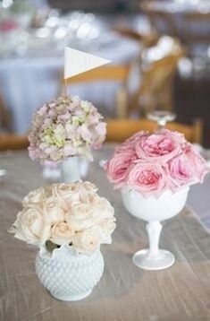 three vases filled with pink and white flowers on top of a dining room table