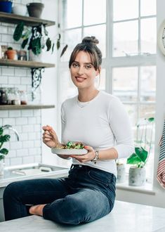 a woman sitting on the kitchen counter holding a plate of food