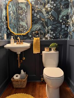 a white toilet sitting next to a sink in a bathroom under a golden framed mirror