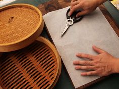 a person cutting paper on top of a wooden table next to a basket and scissors