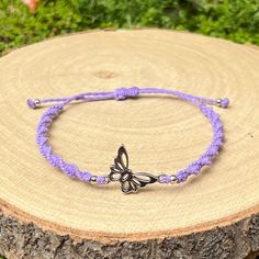 a purple string bracelet with a silver butterfly charm on it sitting on top of a tree stump