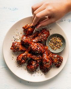 someone is dipping some sauce on top of chicken wings in a white plate with sprinkles