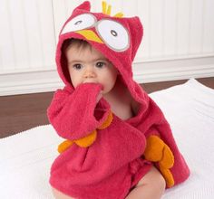 a baby in a pink owl bathrobe sitting on a white towel and covering his mouth