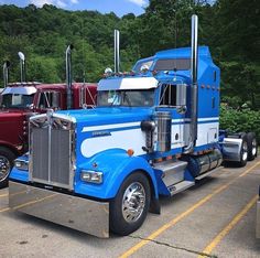 a blue semi truck parked in a parking lot next to other trucks and trees on the side of the road