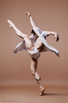 a male ballet dancer in white is posing for the camera with his arms stretched out