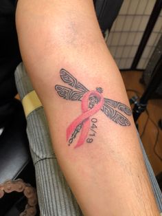 a person with a tattoo on their arm that has a pink ribbon in the shape of a dragonfly