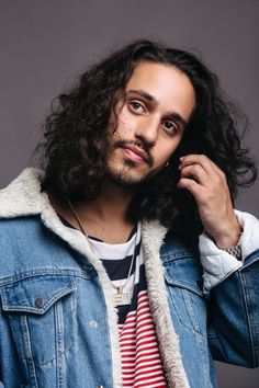 a man with long curly hair wearing a denim jacket and striped shirt is posing for the camera