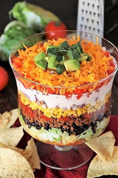 a layered mexican salad in a glass dish with tortilla chips on the side