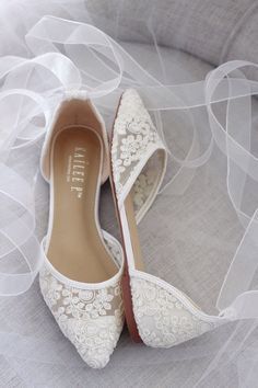 wedding shoes with white lace on them sitting on a bed in front of a veil