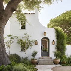 a white house with trees and plants around the front door is featured in this photo