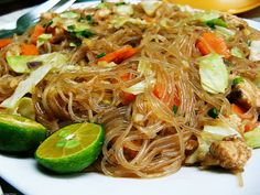 a white plate topped with noodles and veggies next to lime wedges on a table