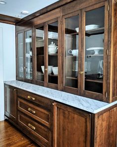 a wooden cabinet with glass doors and marble counter top in a room that has hardwood floors