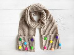 a knitted scarf with multi colored pom poms on the ends and a white background