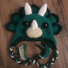 a green crocheted hat with horns and ears on top of a wooden floor