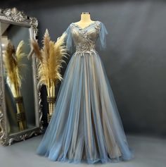 a dress is displayed in front of a mirror and a vase with dried feathers on it