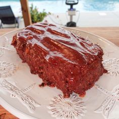 a piece of meatloaf on a white plate next to a glass bowl and water