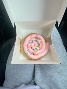 a doughnut with pink frosting and sprinkles in a white box