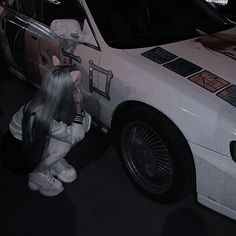 a woman kneeling down next to a parked car