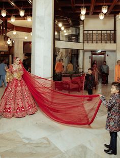 a little boy standing next to a woman in a red dress with a long veil over her head