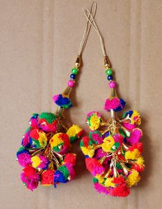 two pairs of colorful pom - poms hanging from hooks on a brown surface