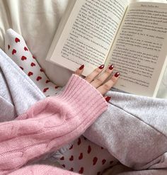 a woman laying in bed with her legs crossed and holding an open book while reading