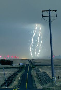 lightning strikes in the sky over an empty road