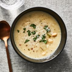 a black bowl filled with soup next to a spoon and glass on a gray surface