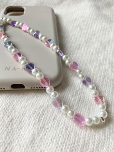 a cell phone with a white and purple beaded necklace next to it's case