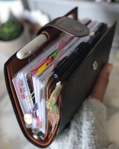 a person holding a wallet with pens and pencils in it