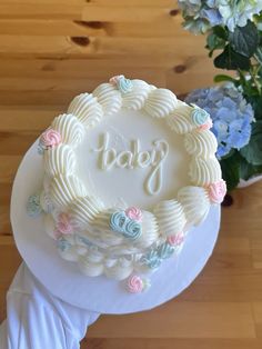 a white cake sitting on top of a table next to blue and pink flowers with the word baby written in frosting