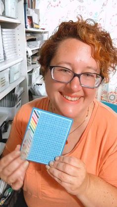 a woman holding up a blue piece of paper in front of her face and smiling at the camera