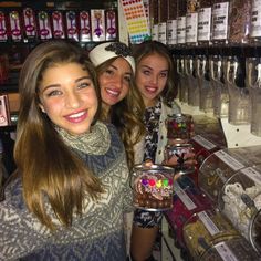 three girls are standing in front of a candy store counter and smiling at the camera