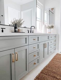 a white bathroom with gray cabinets and gold pulls on the drawers, along with a rug