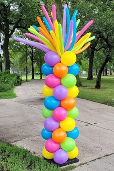 a bunch of balloons that are sitting in the grass near some trees and sidewalks