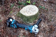 a cordless drill is laying on the ground next to a tree stump