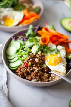 two bowls filled with food on top of a white countertop next to cucumbers and avocado